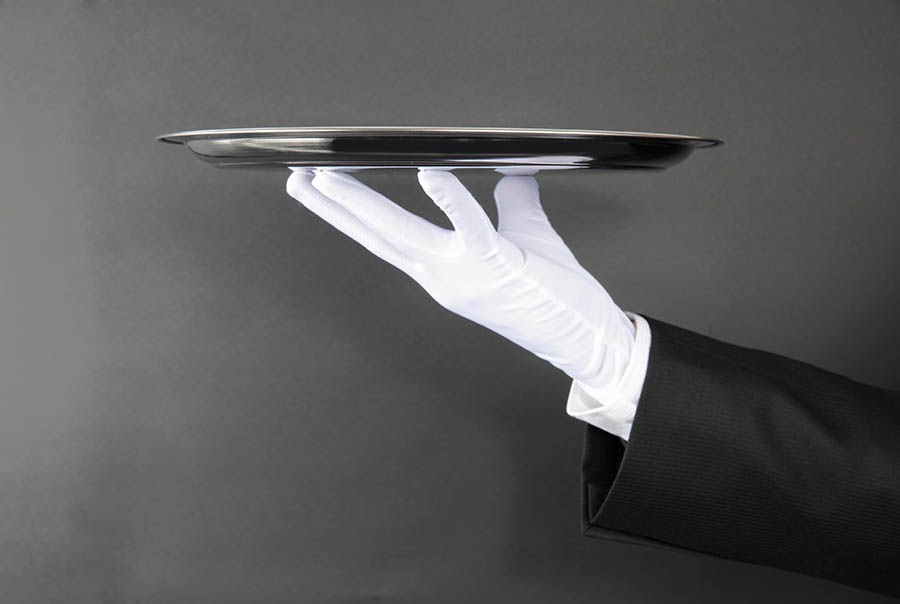 Server with tuxedo and white glove serving on a silver plater