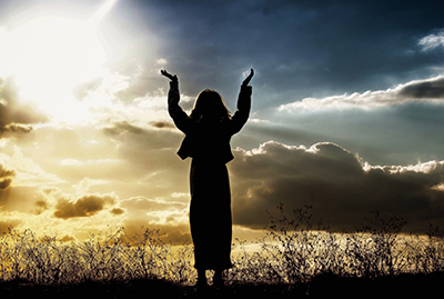 Person with hands raised in air with sun and sky in the background
