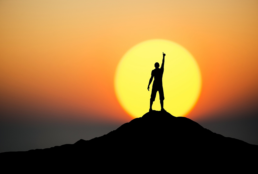 Man standing on top of a mountain infant of a sunset
